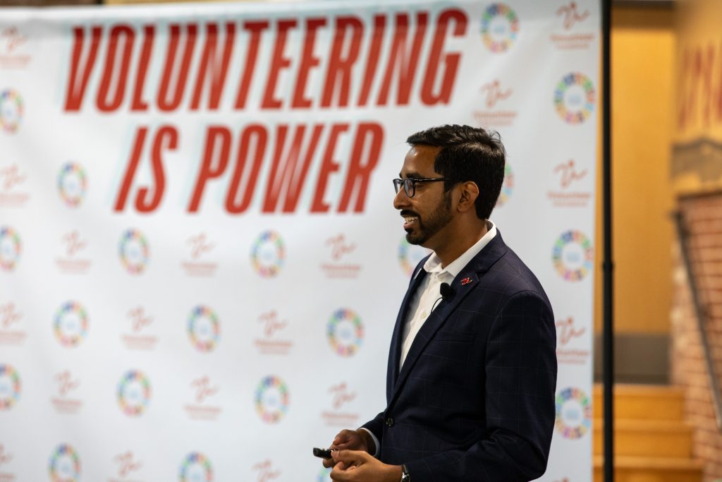 A photo of Nipuna Ambanpola speaking with a faded background showing the words "volunteering is power."