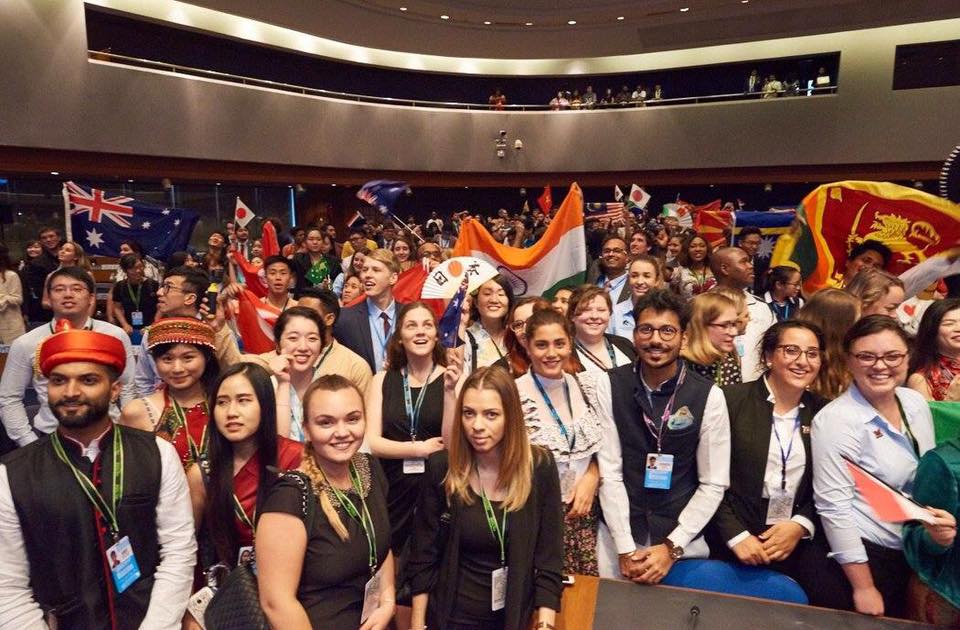 A large group photo of smiling young leaders holding several flags representing multiple countries