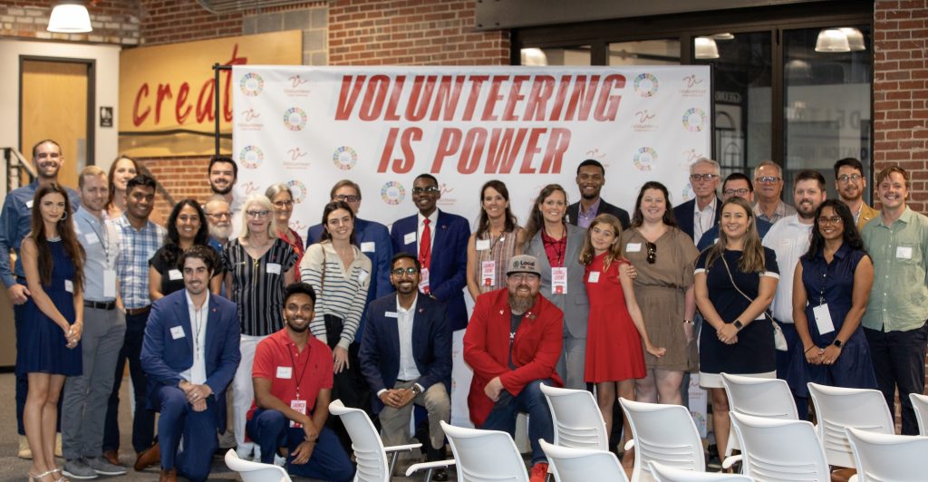 A large group photo with people standing and posing with the backdrop reading "volunteering is power."